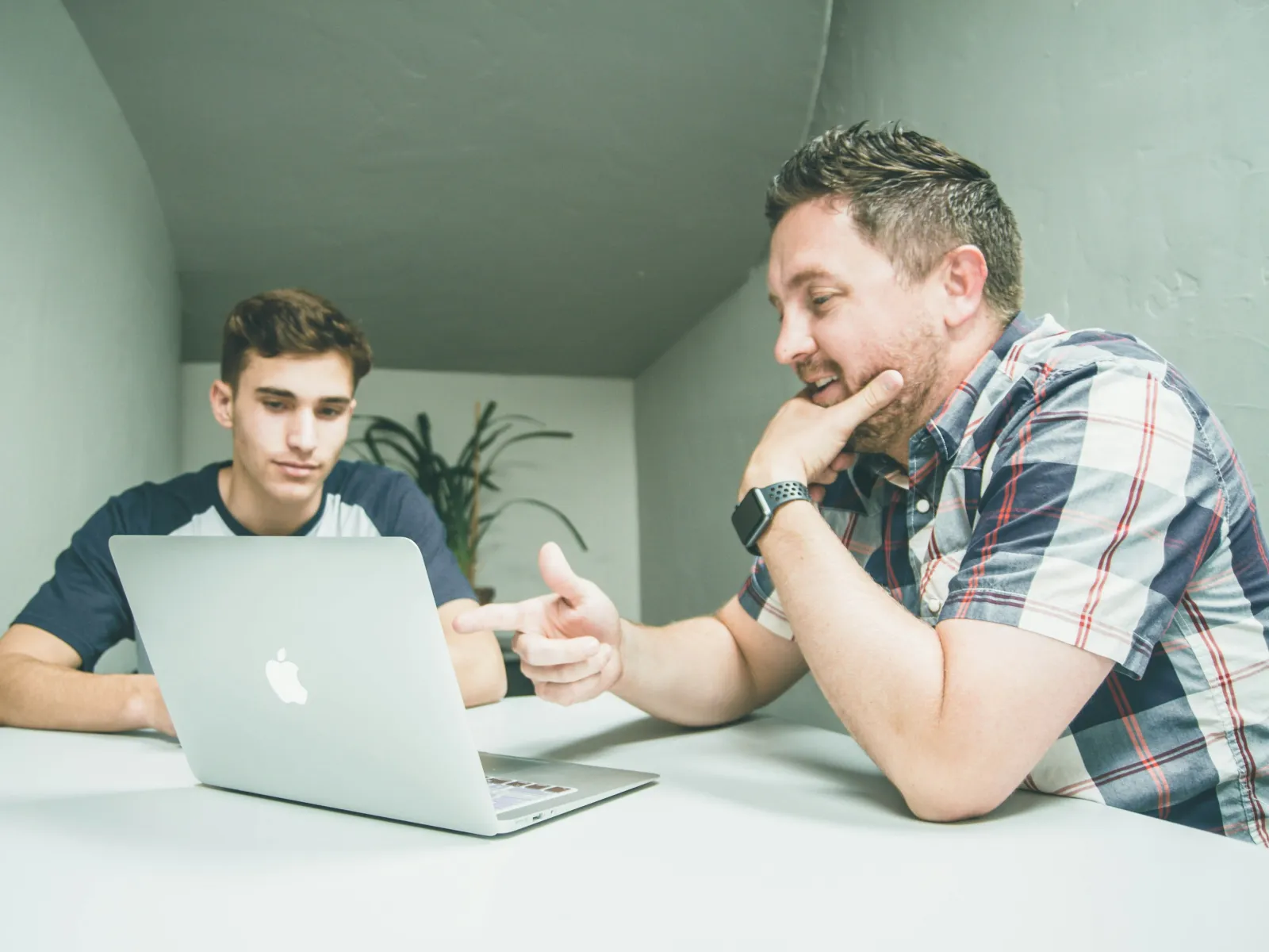 a couple of men sitting at a table looking at a laptop