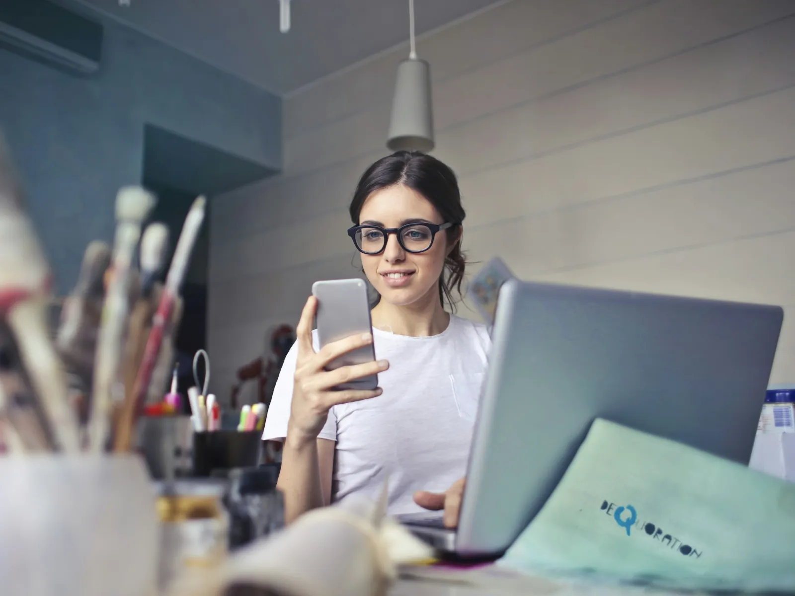 a person holding a phone and looking at a laptop