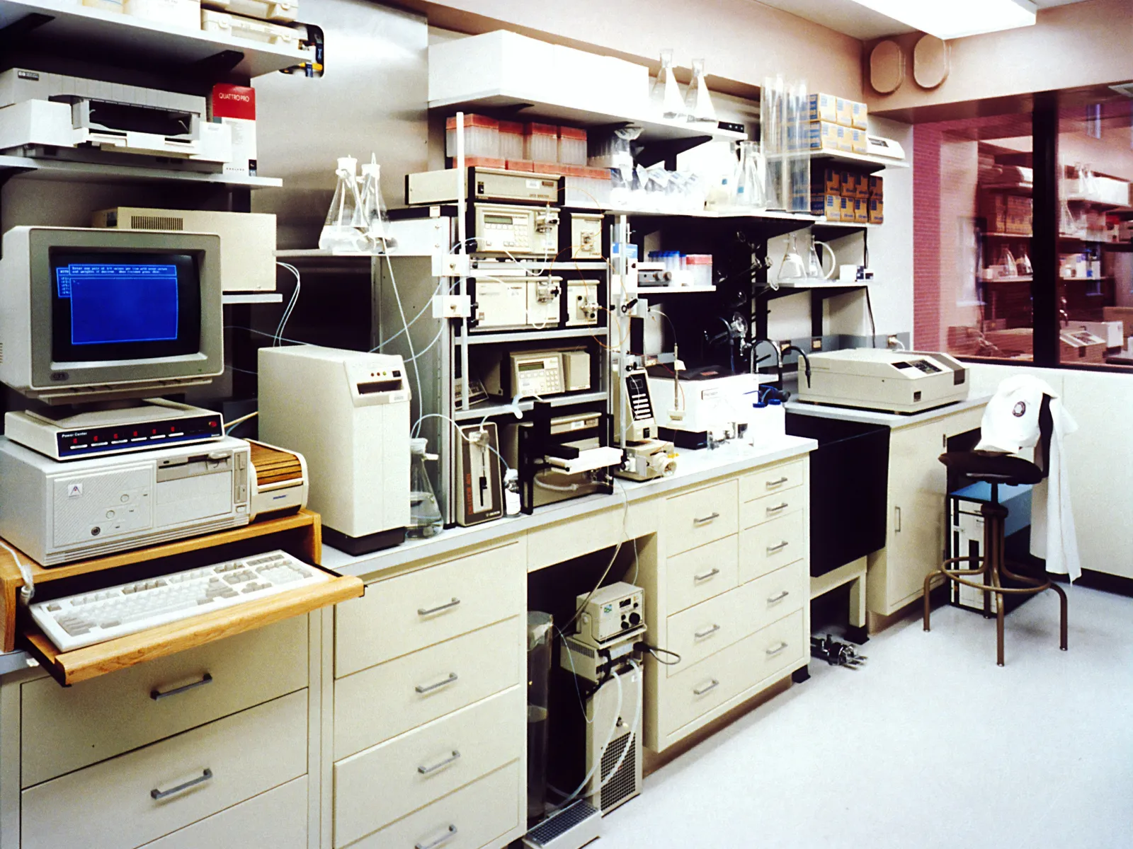 Vintage laboratory with early computer, scientific instruments, glassware, and lab equipment on countertops and shelves.