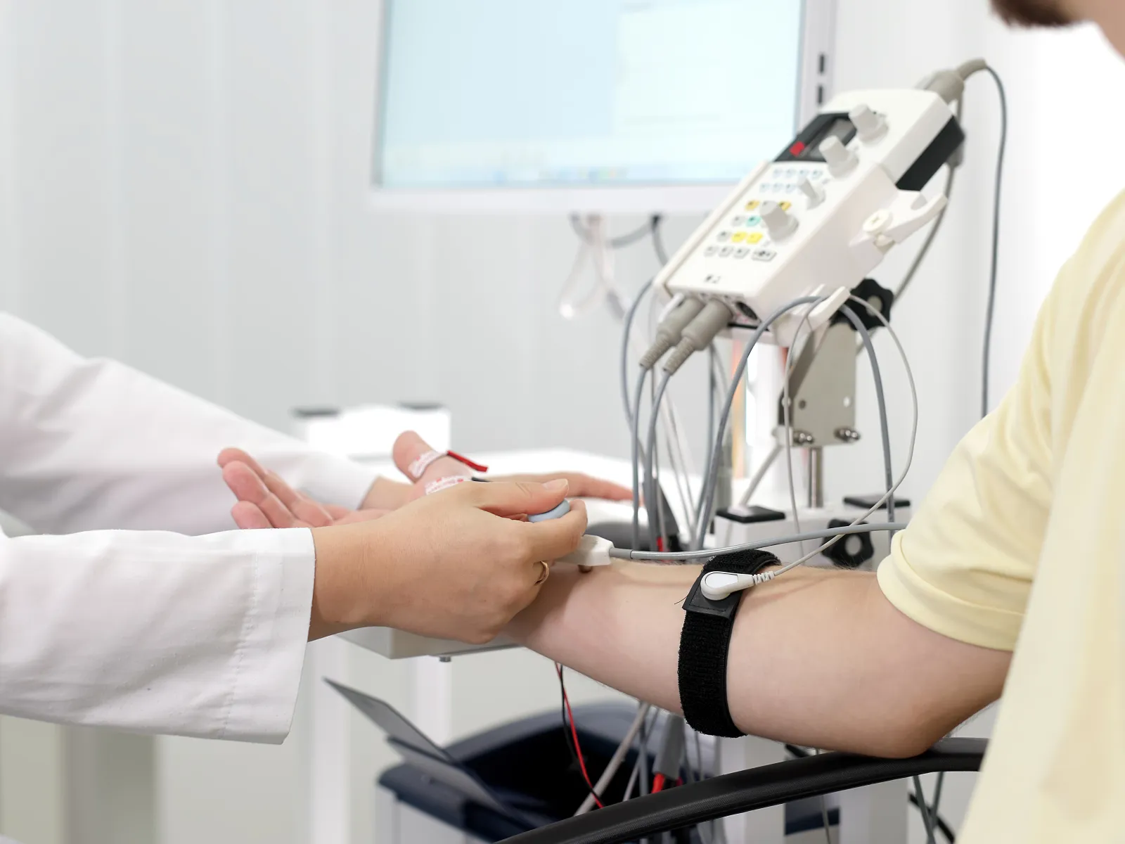 Healthcare professional conducting nerve conduction study on patient's arm using medical diagnostic equipment.