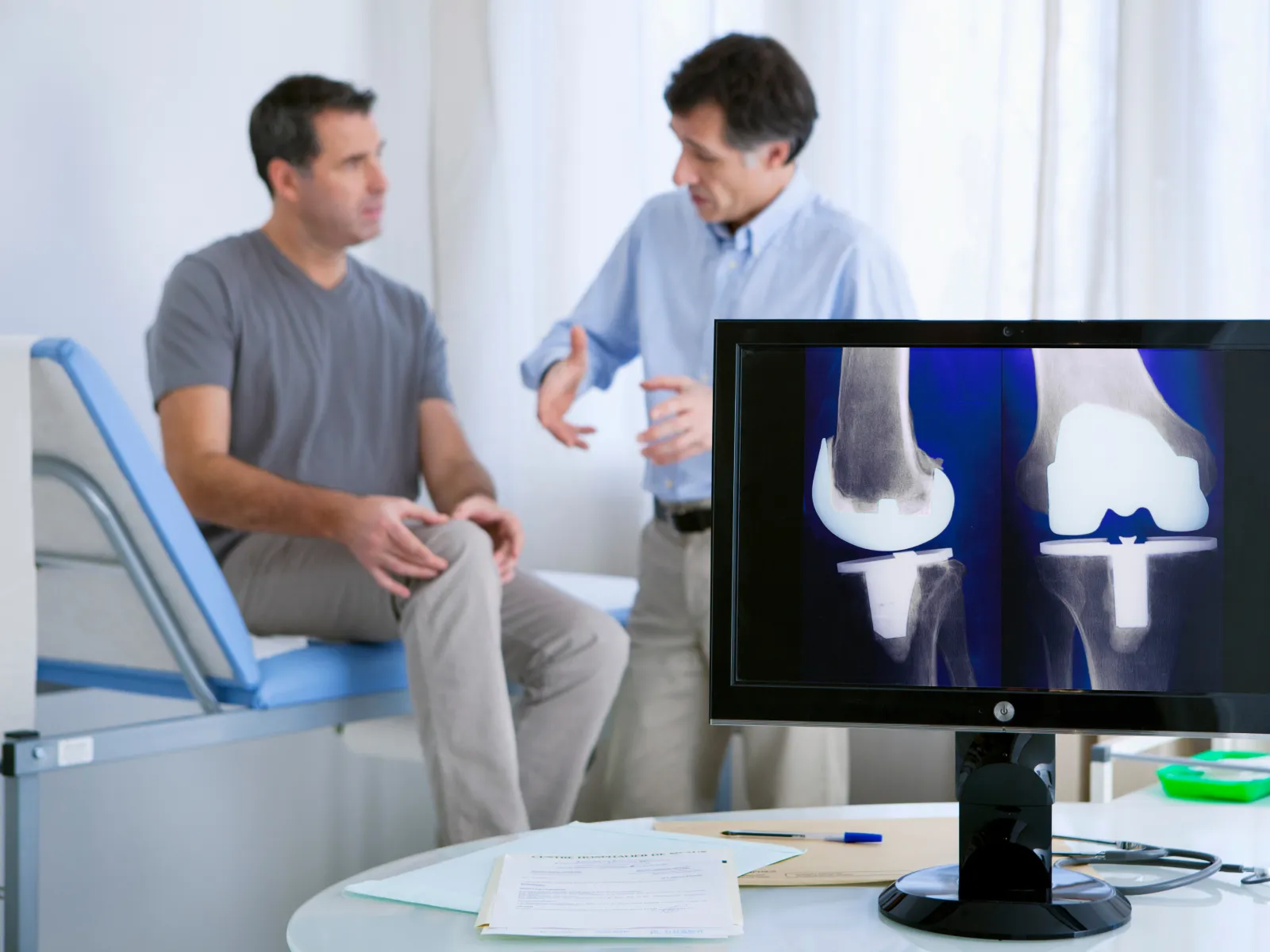 Doctor consulting male patient with knee pain and showing knee X-ray on monitor in medical clinic.