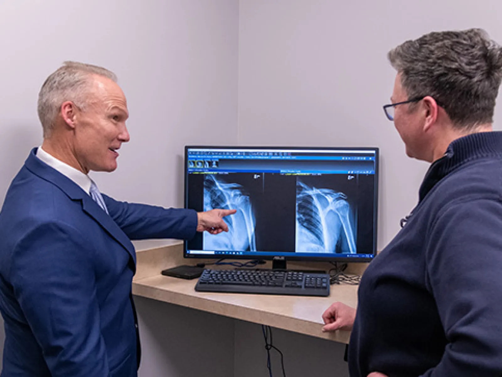 Doctor explaining shoulder X-ray images on computer monitor to patient in a medical office.
