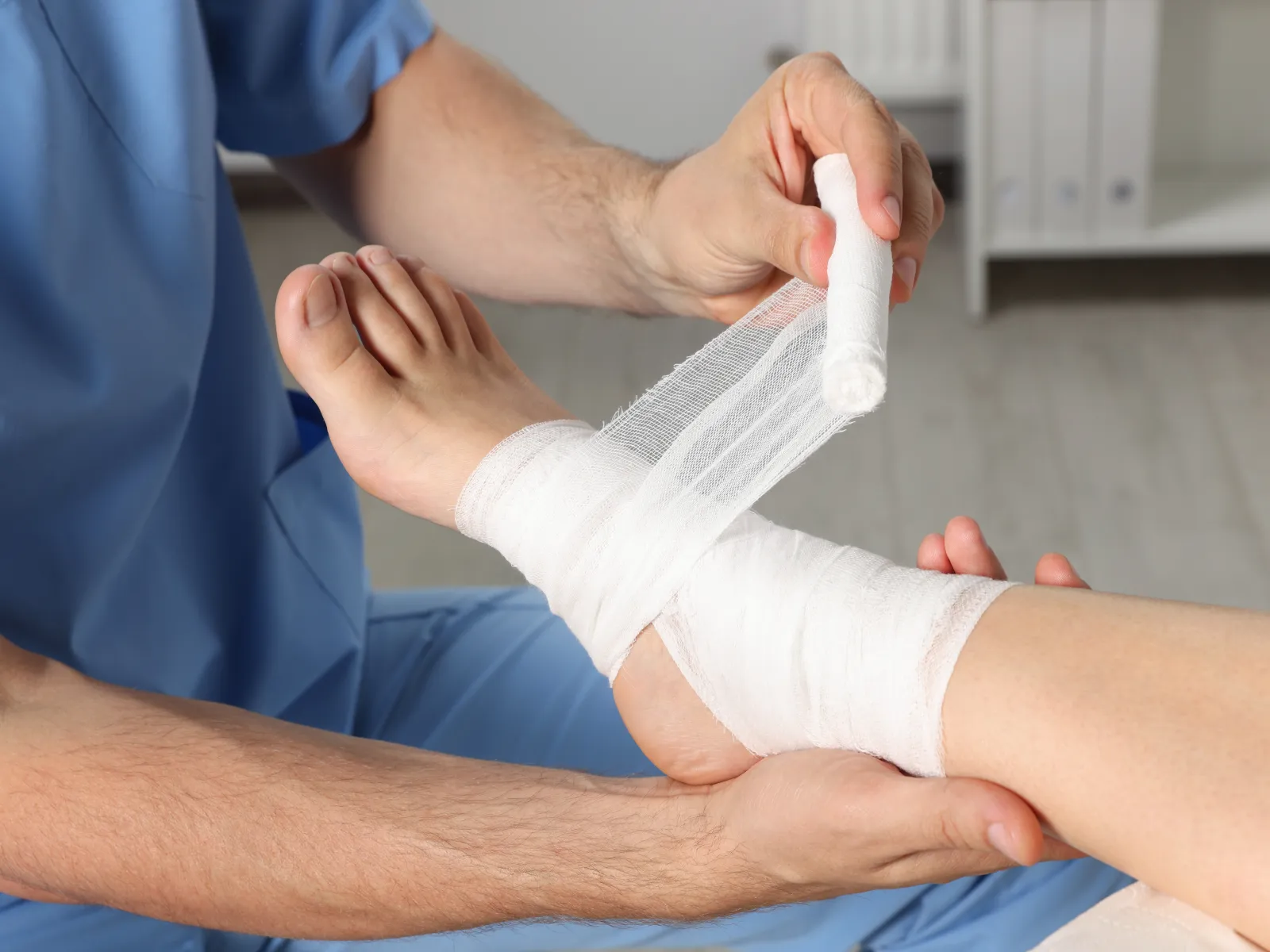 Medical professional wrapping patient's ankle with a white bandage in a clinical setting.