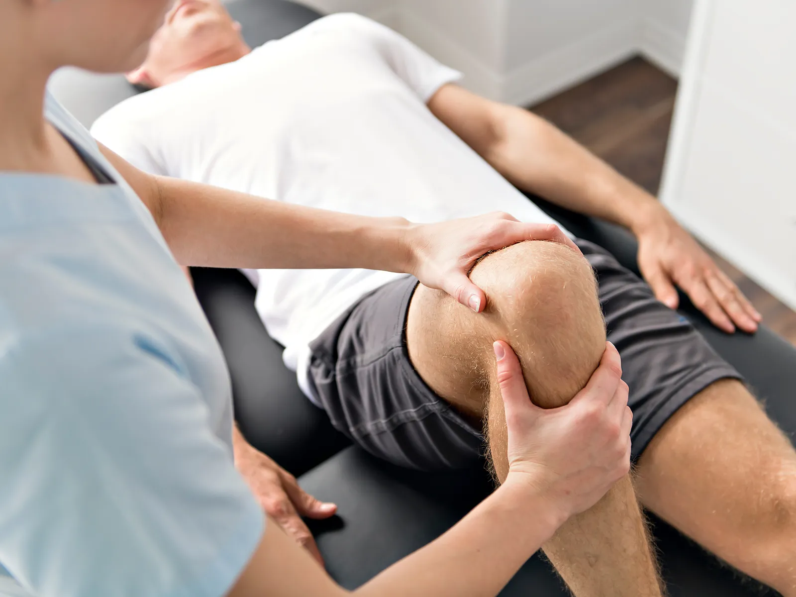 Physical therapist examining and stretching a patient's knee during rehabilitation therapy session.