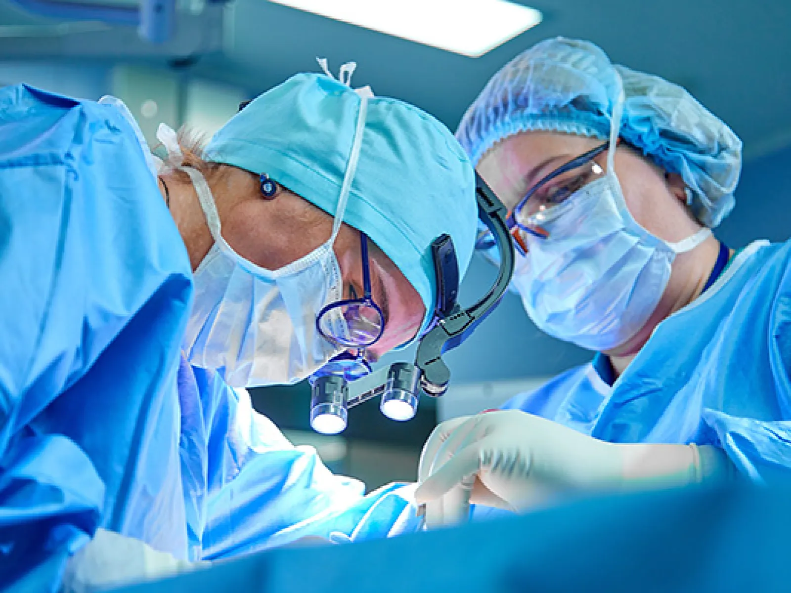Two surgeons wearing surgical masks and blue scrubs performing an operation in a sterile operating room.