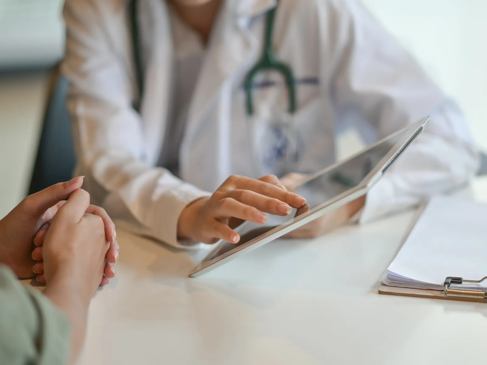 Doctor consulting patient using digital tablet with clipboard on table in medical office