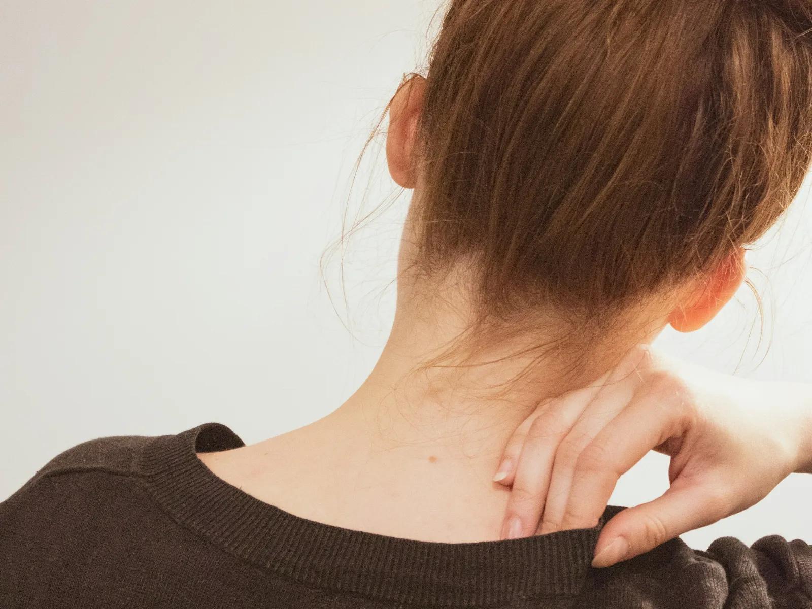 Woman with red hair tied up in a bun scratching her neck wearing a dark sweater against a plain background.