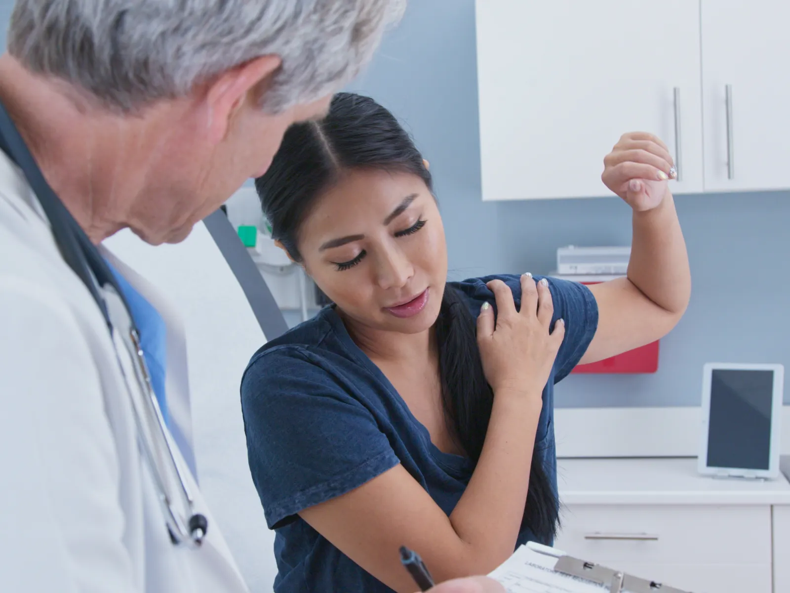 Doctor examining woman complaining of shoulder pain in a medical office during consultation.