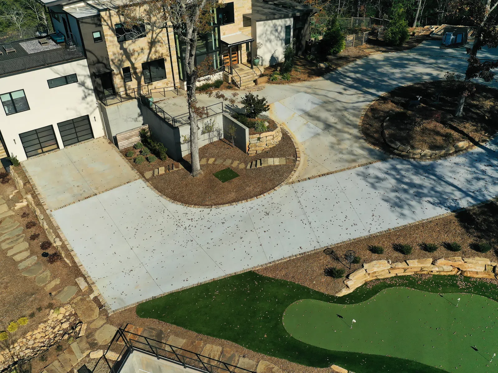 Aerial view of modern house with large driveway, landscaped garden, and a small golf putting green.