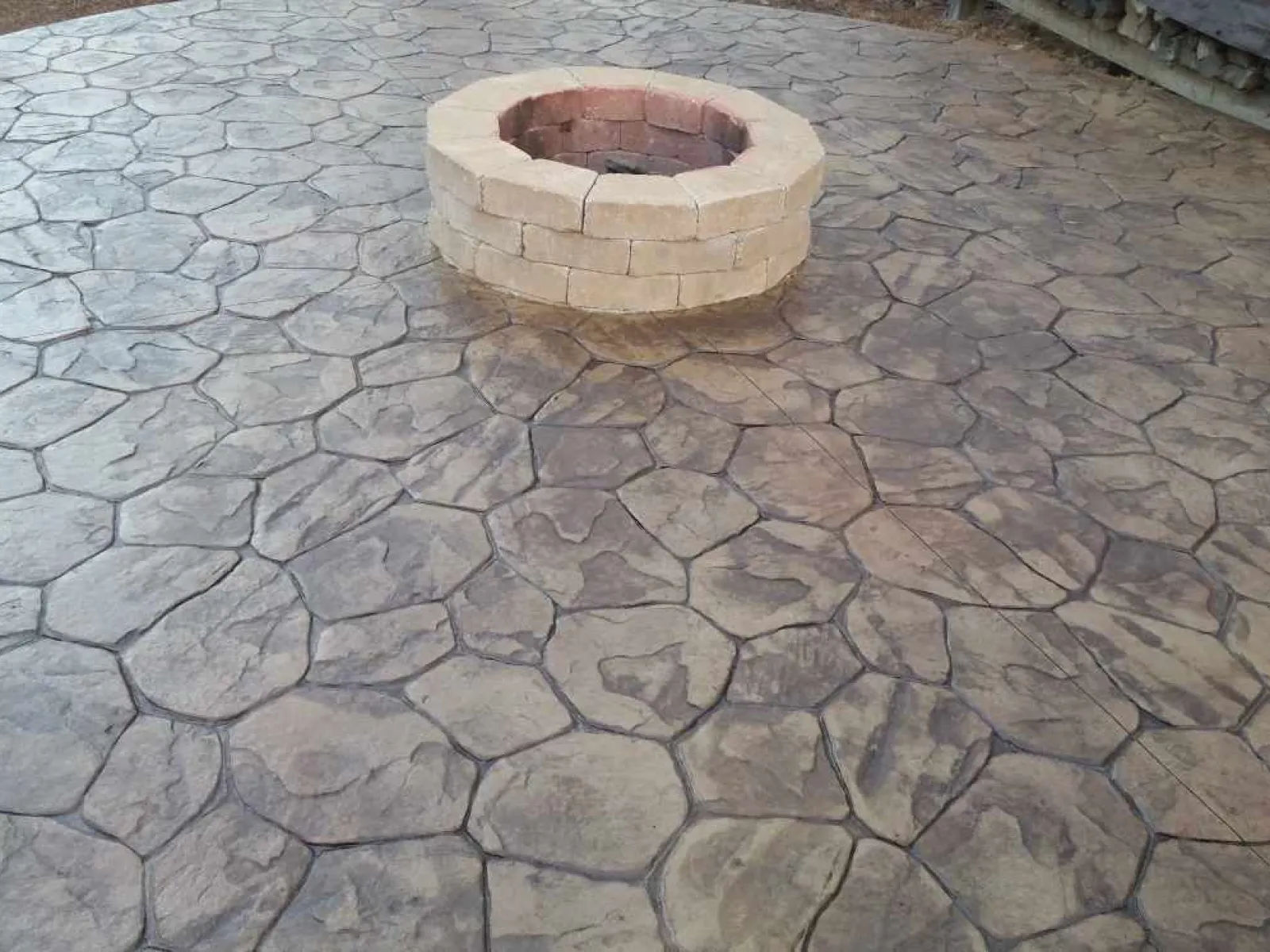 Round stone fire pit on decorative stamped concrete patio with irregular stone pattern and earth tones