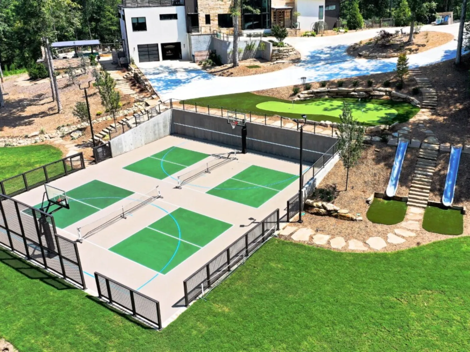Aerial view of a vibrant sports court with basketball hoops, slides, and a green landscape.