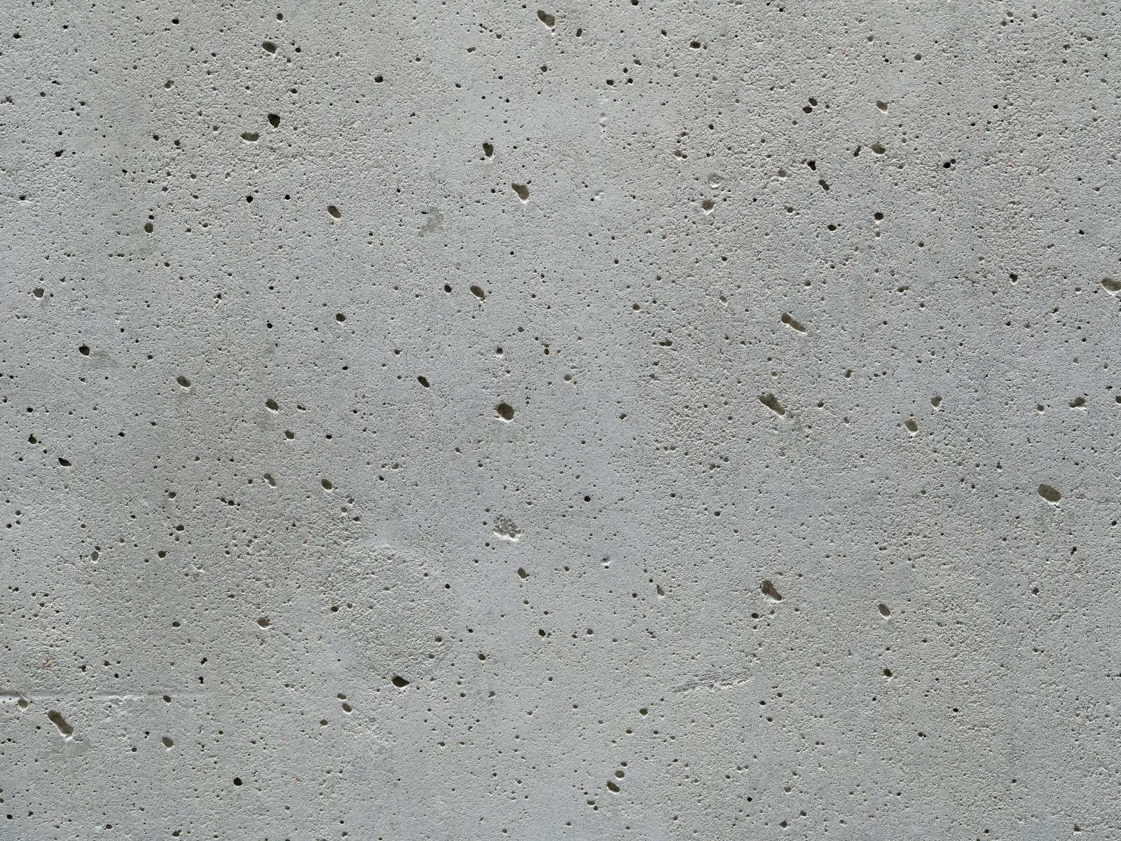 Close-up of gray concrete surface with small holes and rough texture under natural light