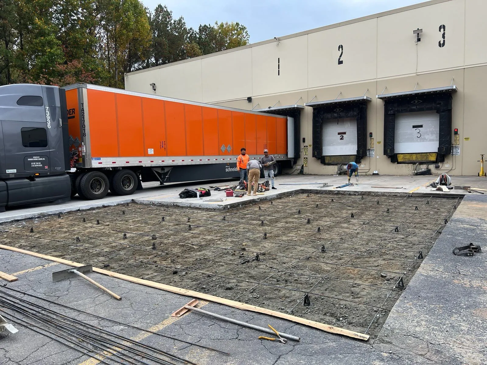Construction workers laying concrete for loading dock with a large truck parked nearby.