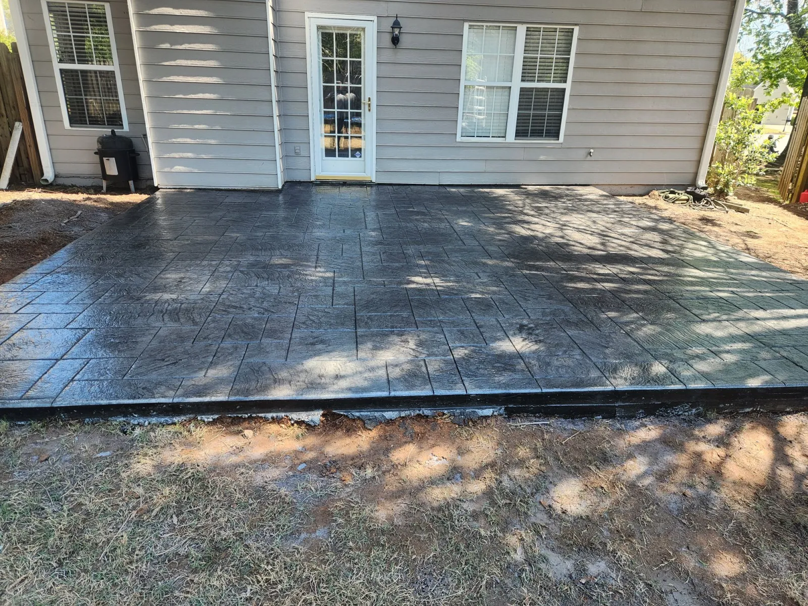 Newly installed stamped concrete patio behind a house, showcasing a stylish finish and natural lighting.