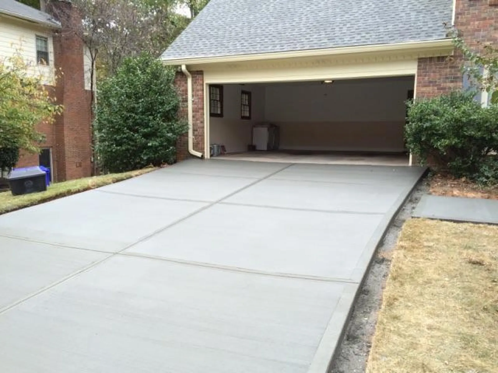 Freshly poured concrete driveway leading to a garage, surrounded by green shrubs and grassy area.