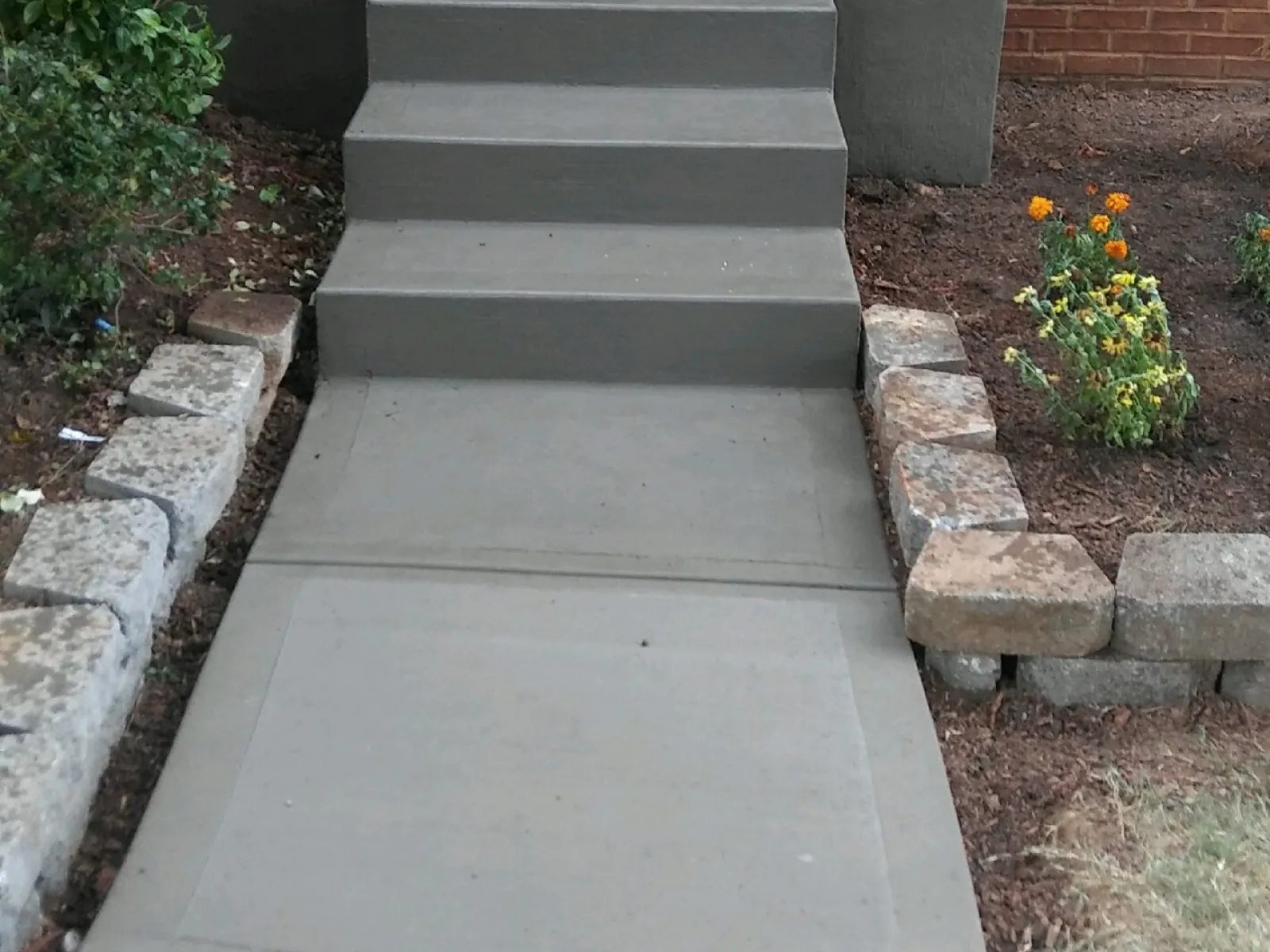 Freshly poured concrete steps and walkway leading to a front door, surrounded by landscaping.