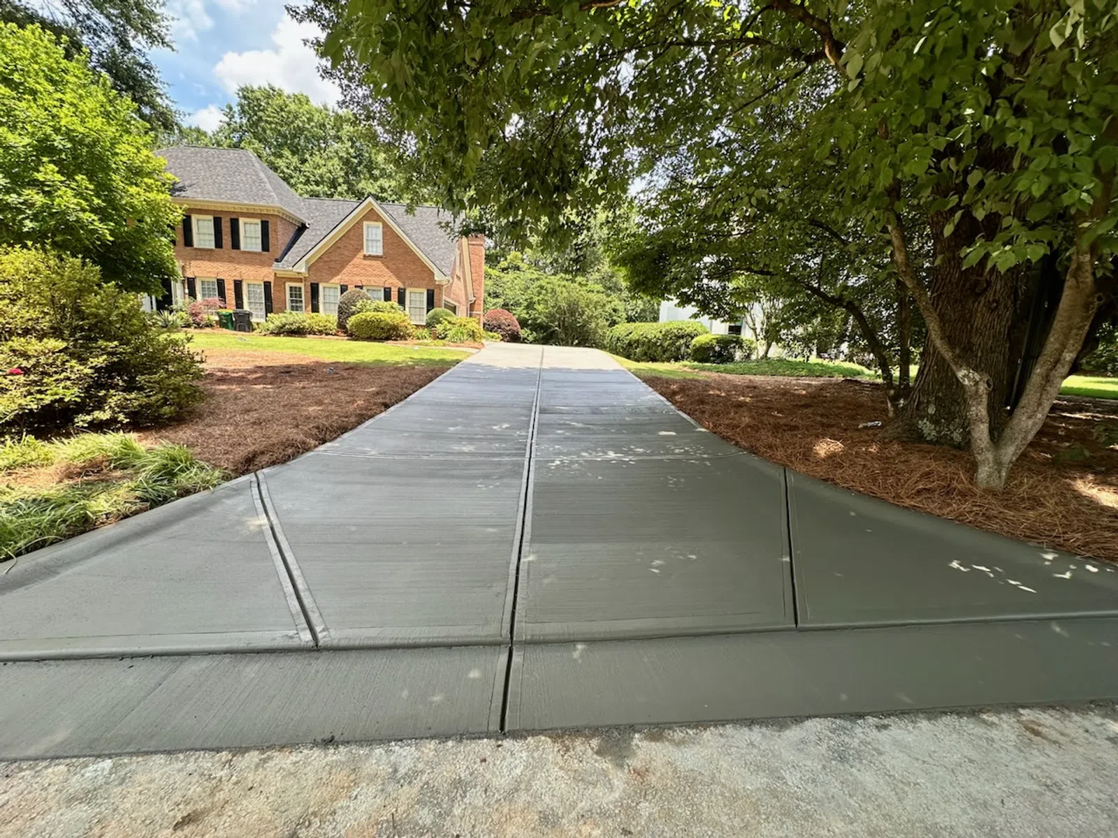 Smoothly paved concrete driveway leading to a two-story brick house surrounded by trees and landscaping.