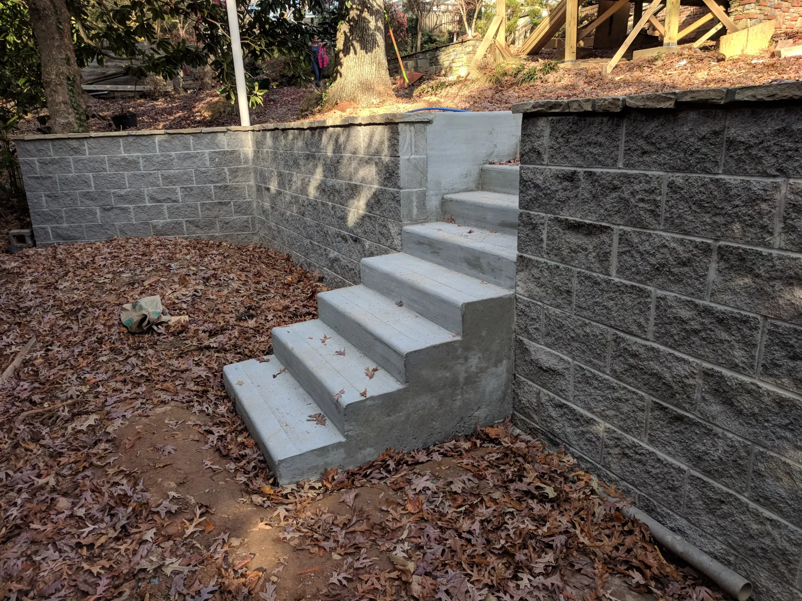 Concrete stairs amid stone retaining walls surrounded by fallen autumn leaves in a backyard setting.