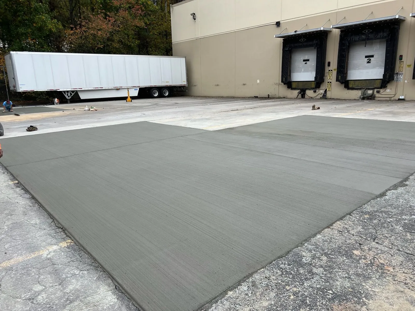 Freshly laid concrete surface in a loading dock area with delivery trucks in the background.