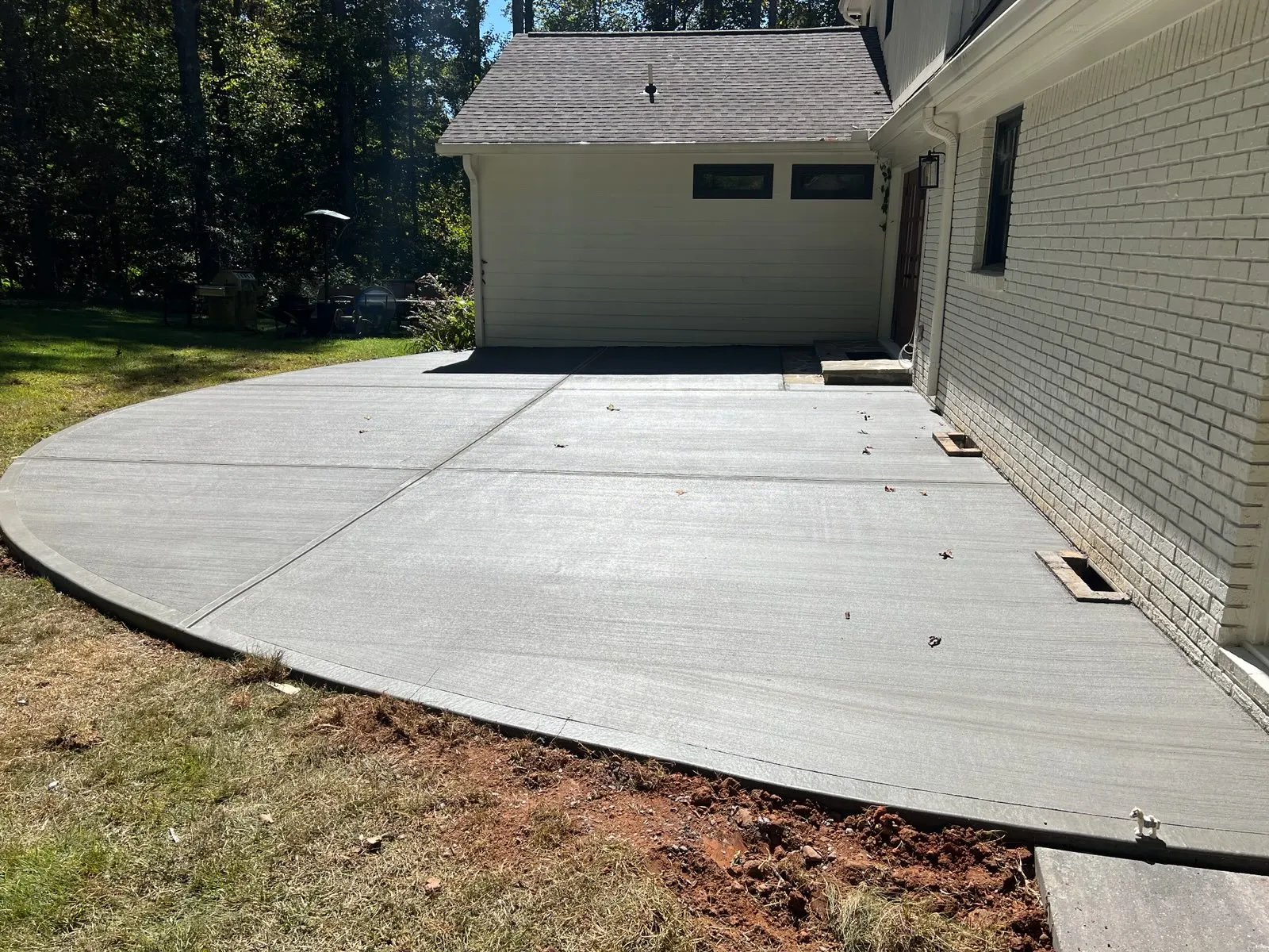 Freshly poured concrete patio extending from a house, surrounded by grass and trees in a serene backyard setting.