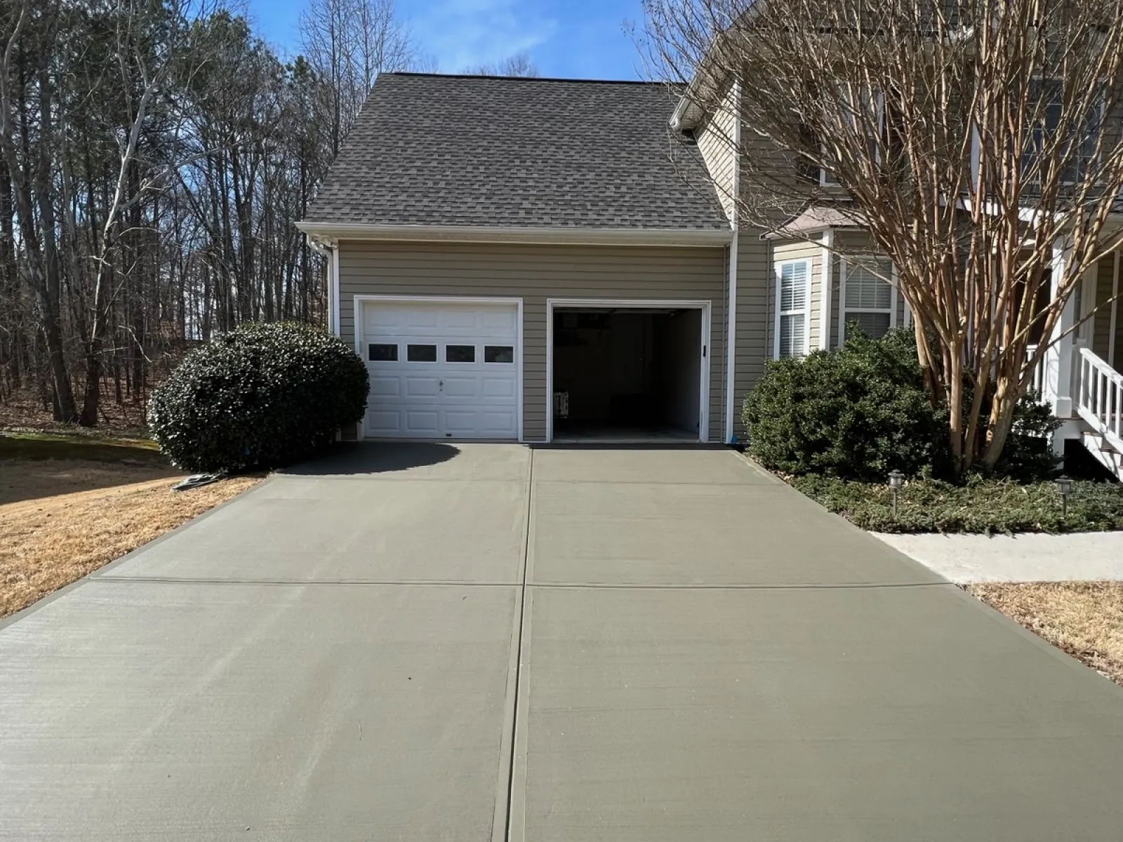 Freshly poured smooth concrete driveway leading to a two-car garage attached to a beige house.