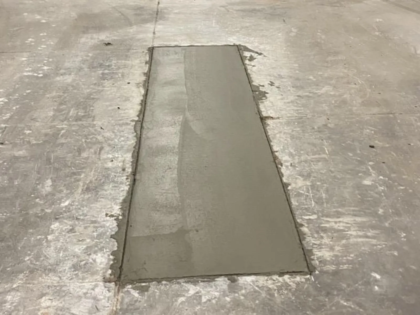 Freshly poured concrete patches on a warehouse floor with shelves in the background and tools nearby.