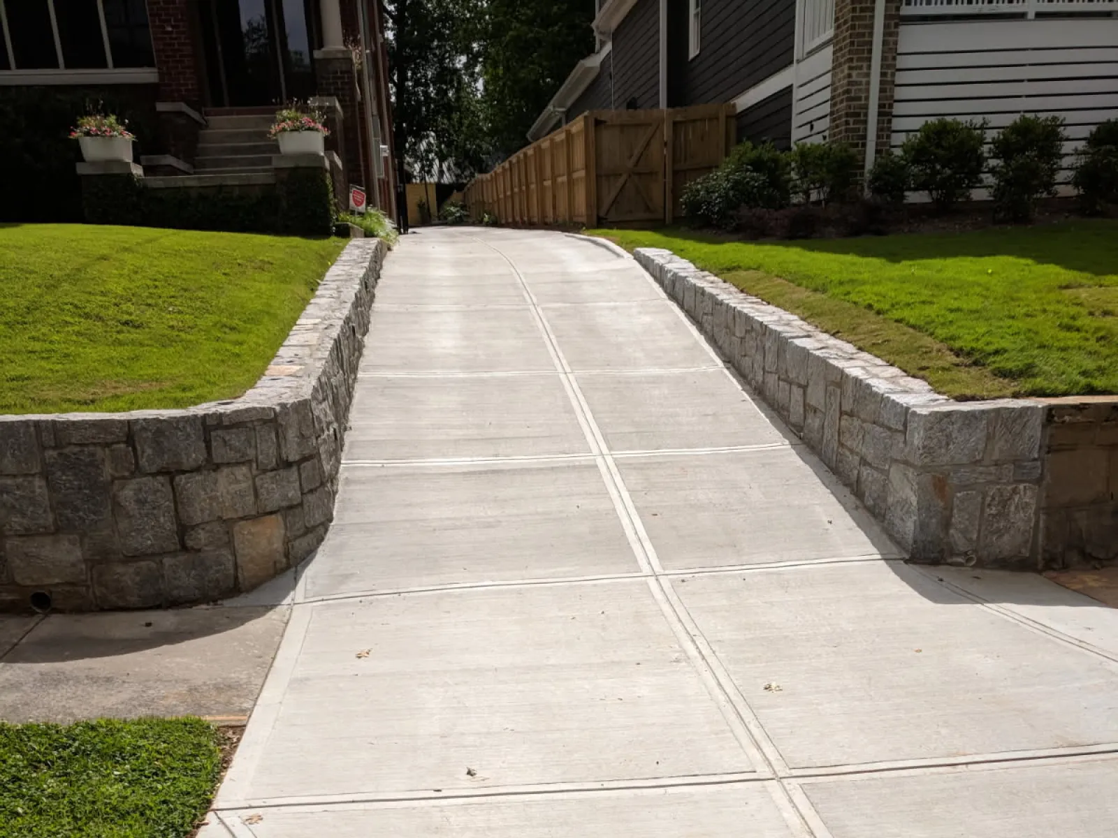 New concrete driveway flanked by stone retaining walls and green lawns in a residential neighborhood.