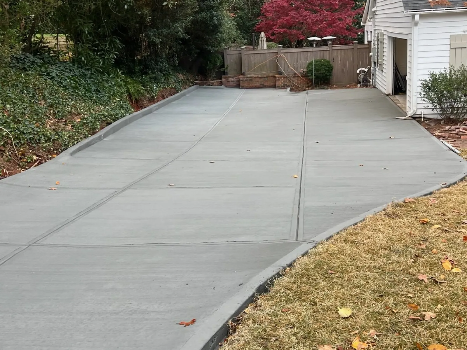 Newly poured concrete driveway beside white house surrounded by trees with autumn foliage.