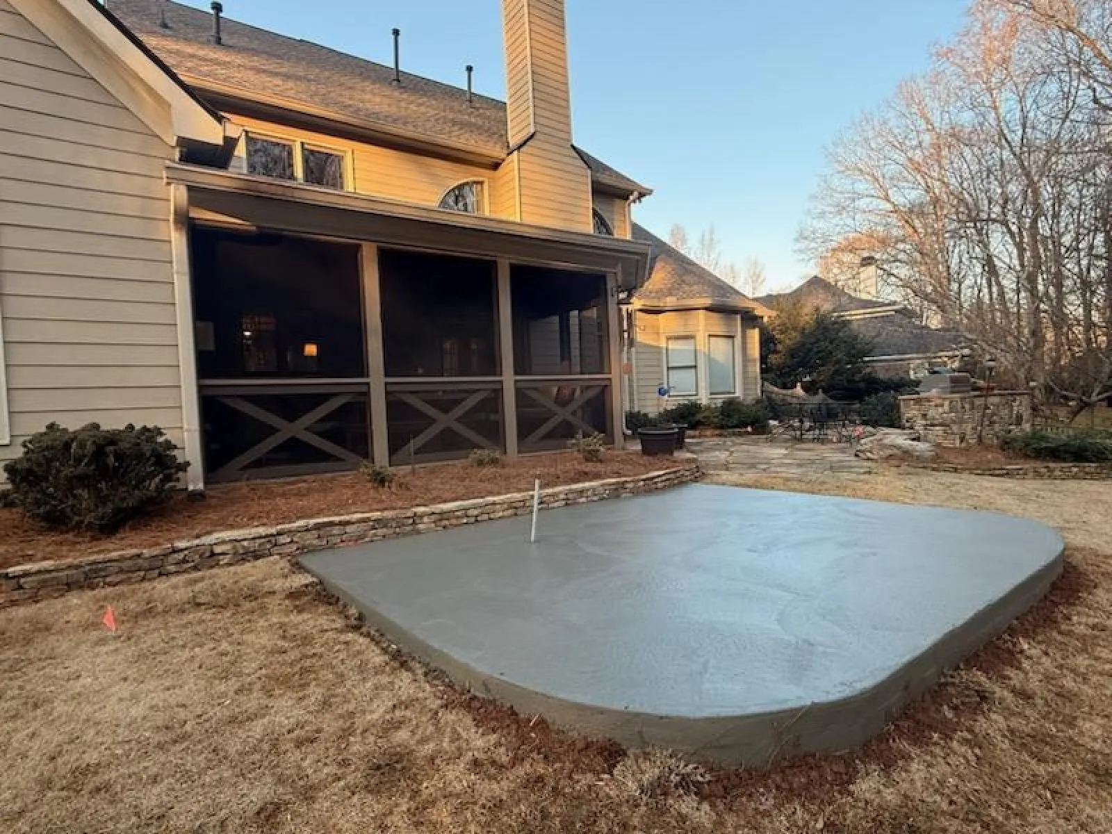 Newly poured concrete patio slab beside a beige house with screened porch and dry grass yard