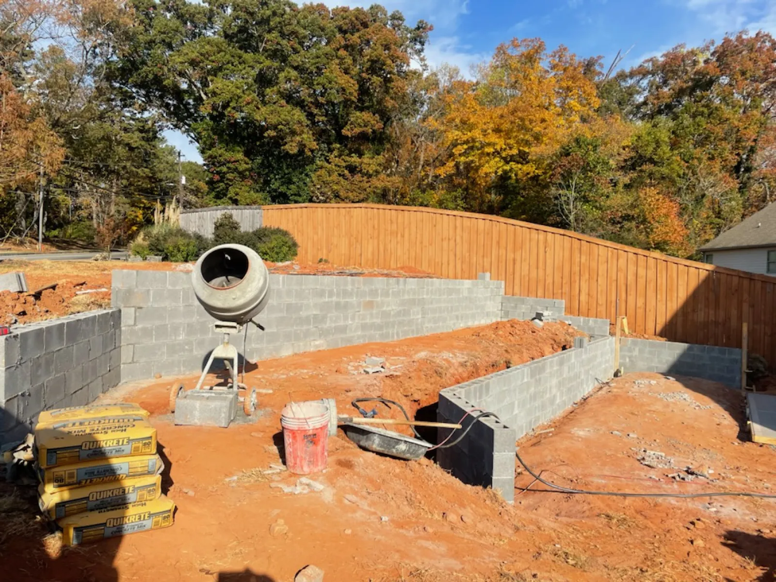 Construction site showing a cement mixer, block wall foundation, and autumn landscape in the background.