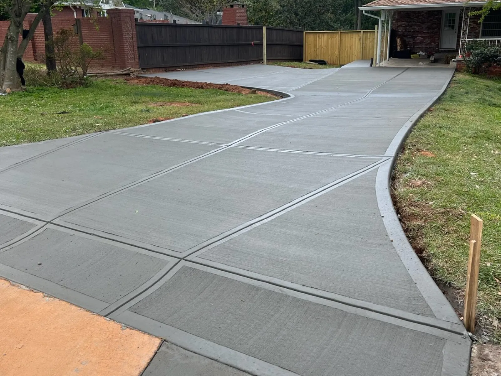 Newly poured concrete driveway leading to a home with smooth finish and sectioned joints under blue sky.