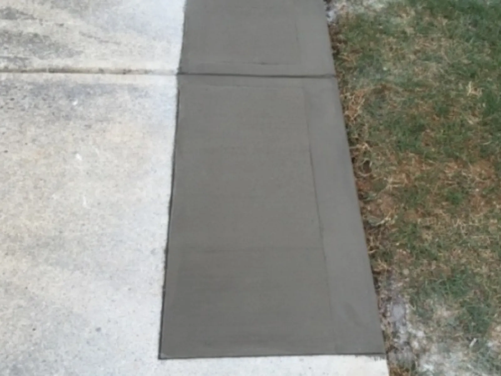 Freshly poured concrete slab laid on a driveway with grassy edges, showcasing smooth surface finish.