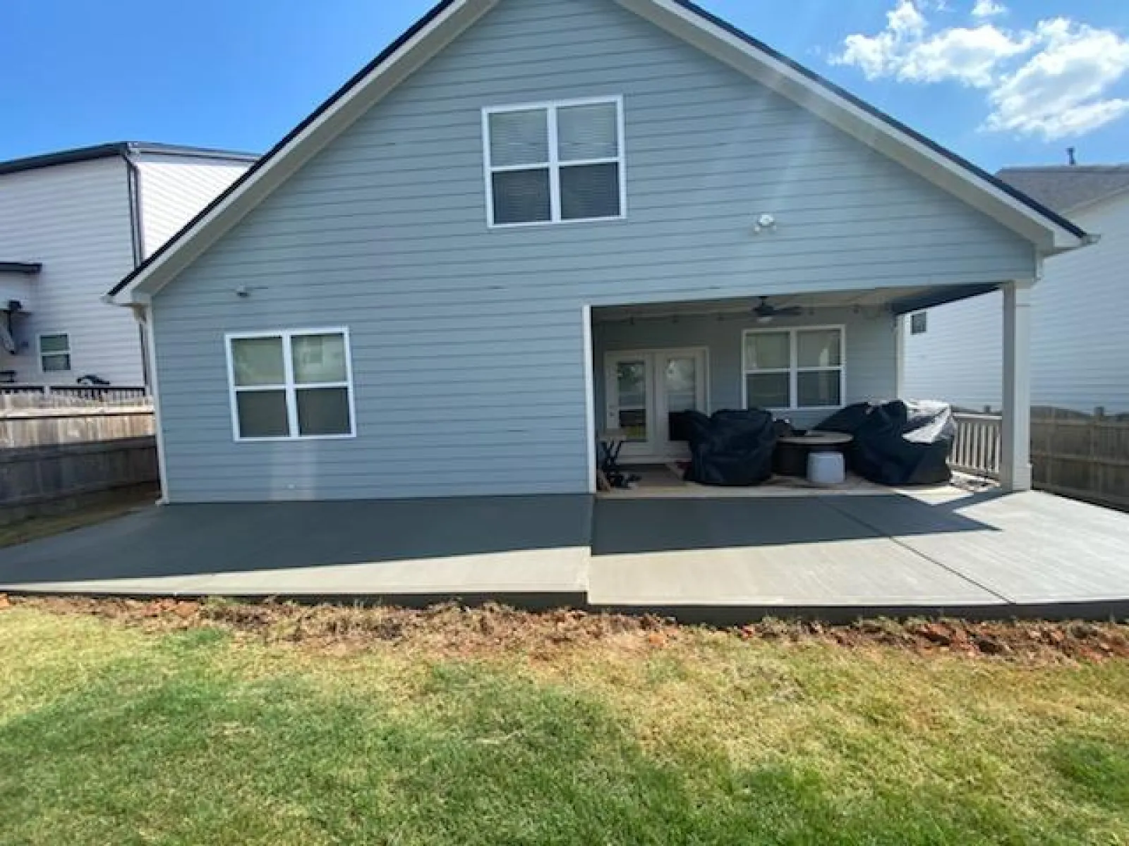 Spacious backyard patio area with gray concrete and seating under a covered porch.