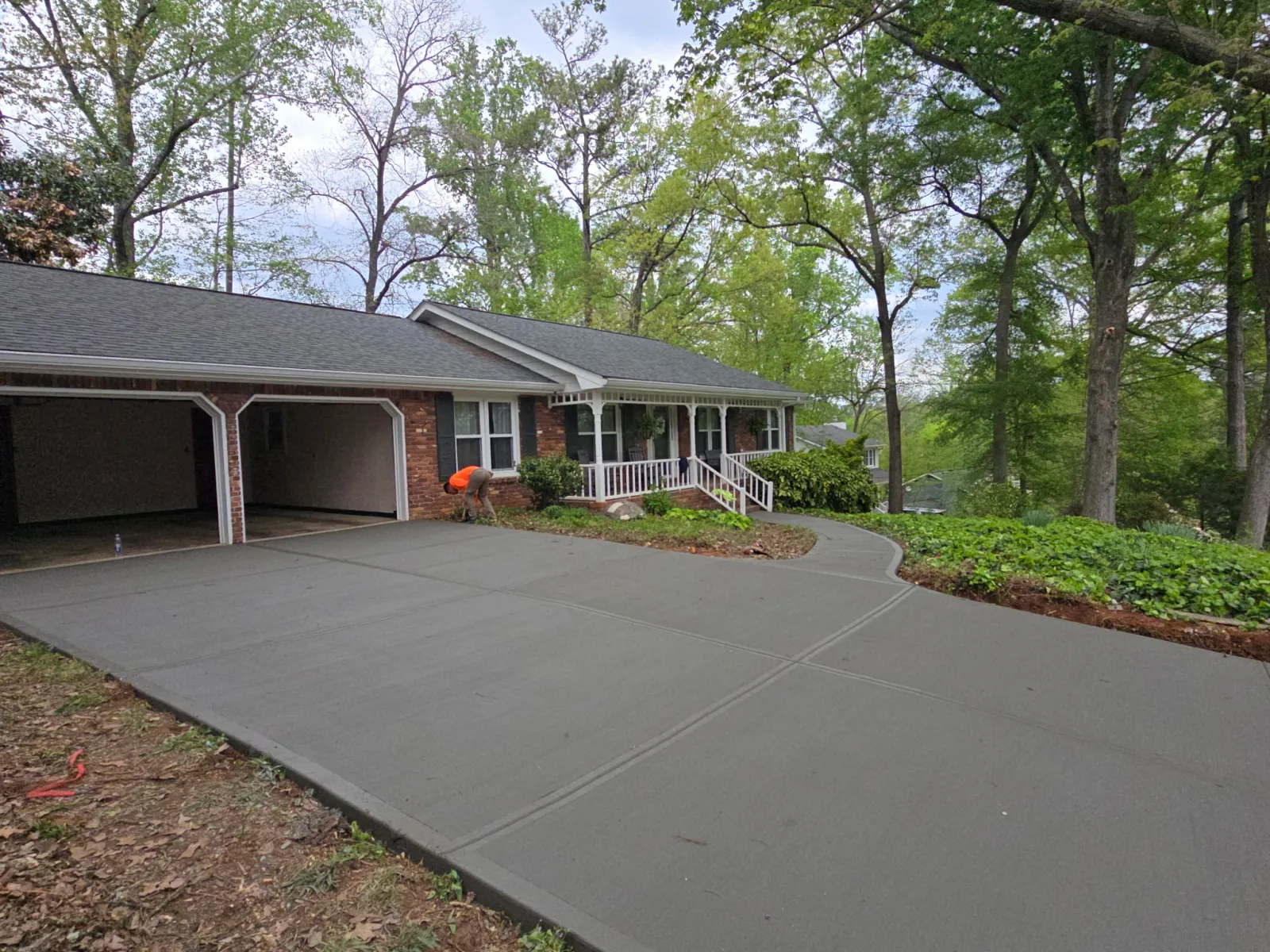Newly poured smooth concrete driveway leading to a brick house with an open garage and surrounding trees.
