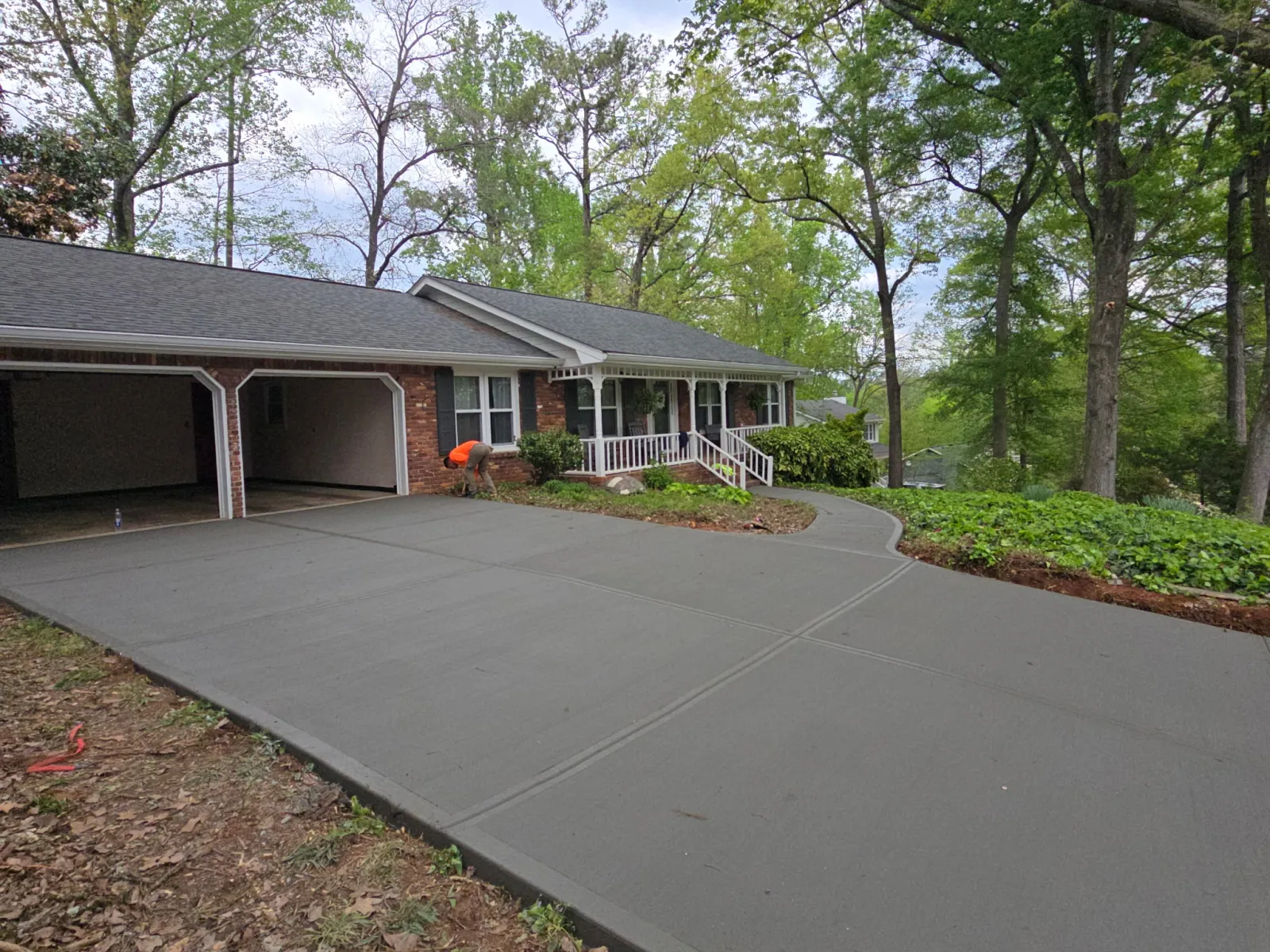 Newly poured smooth concrete driveway leading to a brick house with an open garage and surrounding trees.