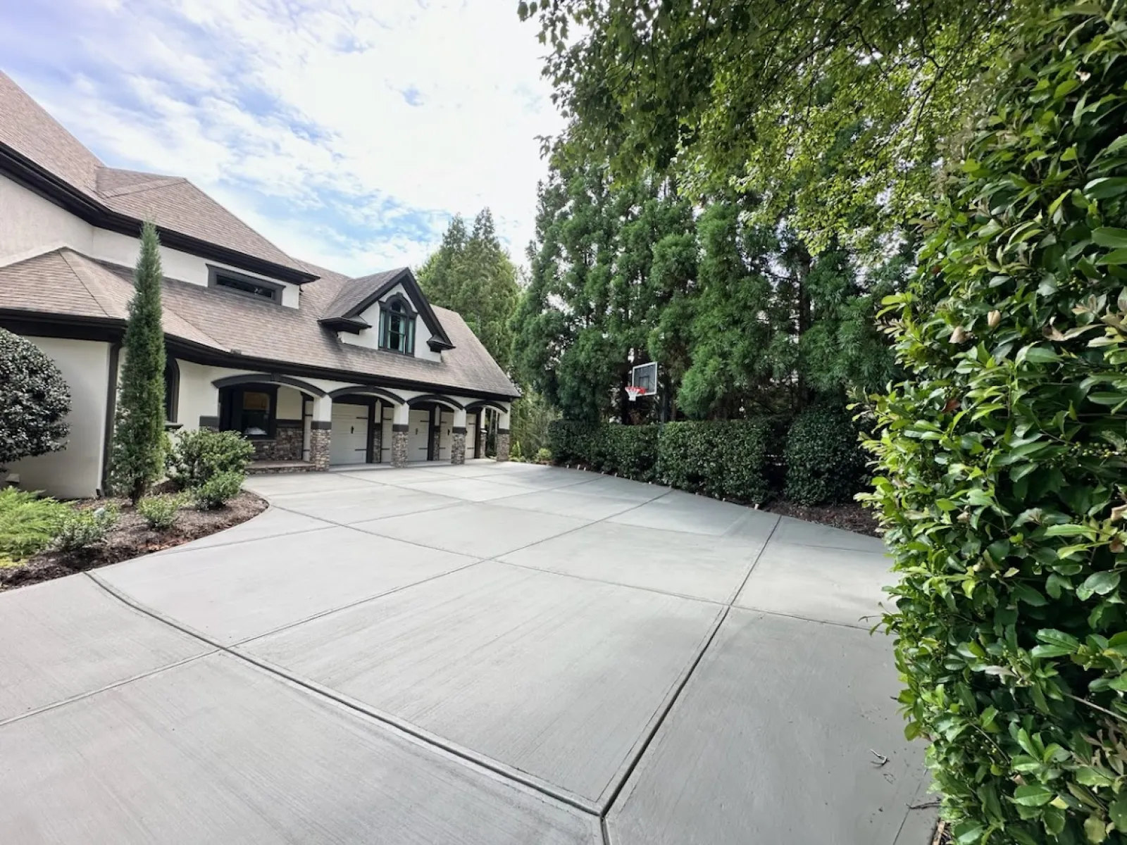 Spacious driveway leading to a beautiful home, surrounded by lush greenery and trees under a cloudy sky.