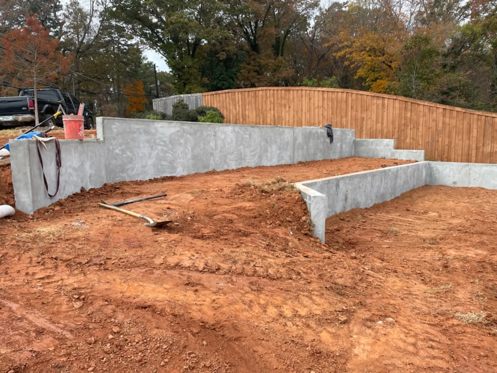 Concrete retaining walls surround freshly excavated red soil with tools nearby in a residential backyard.
