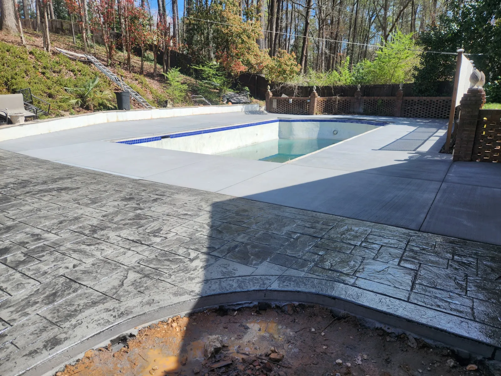 Renovated backyard pool area with fresh concrete and stamped designs surrounded by lush greenery.