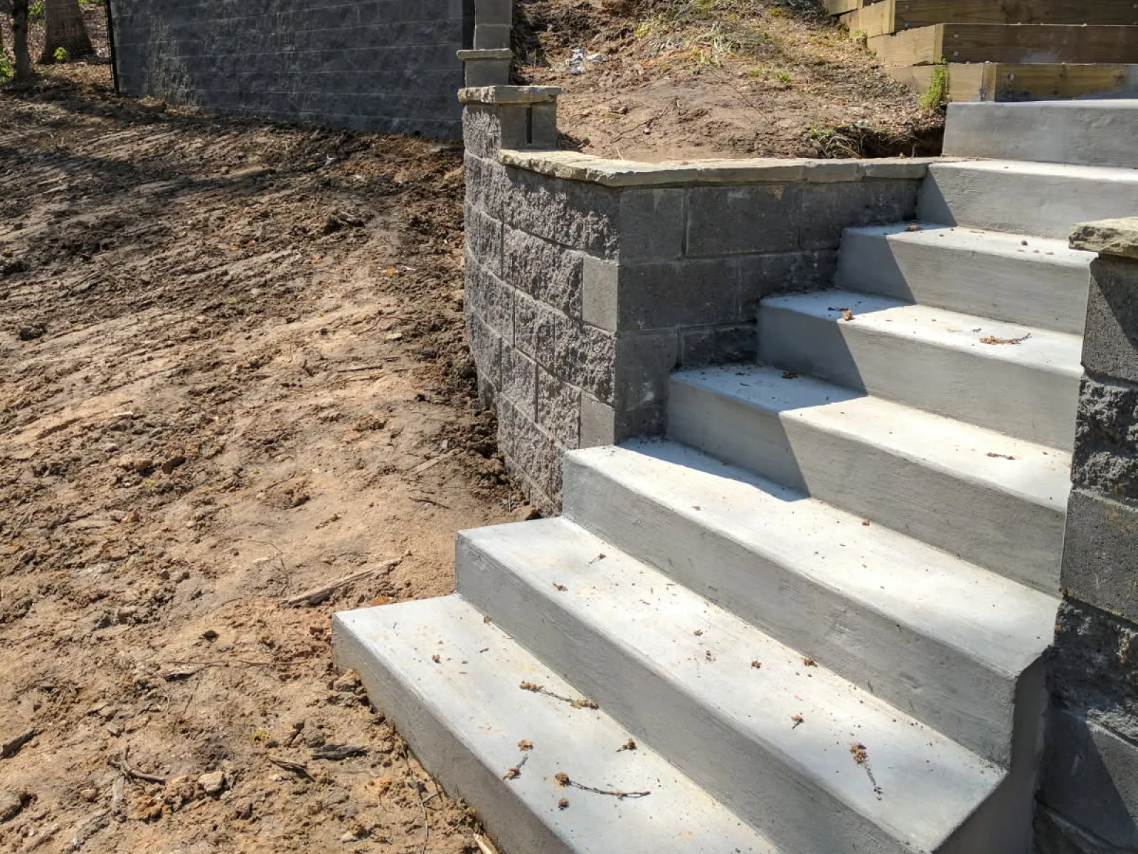 Outdoor concrete stairs leading up a slope with retaining walls and wooden steps in a wooded residential backyard.