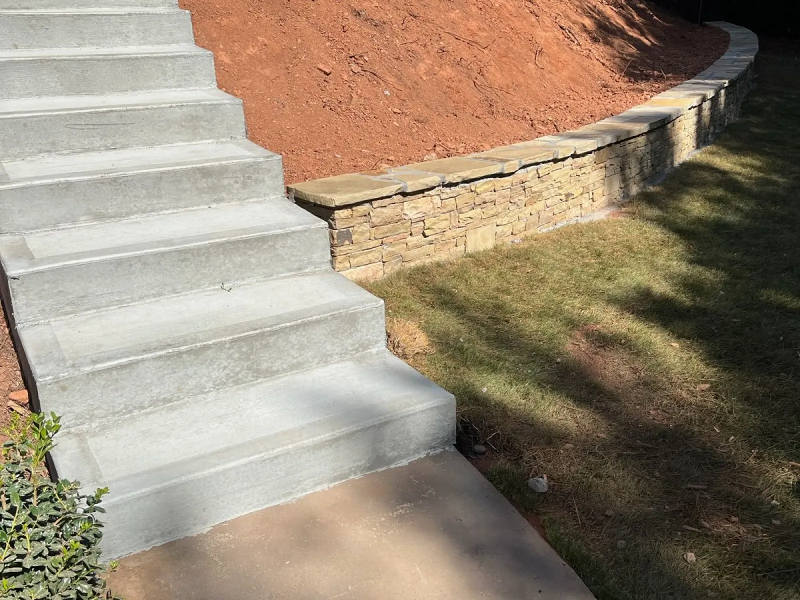 Concrete steps leading to a landscaped hill with stone retaining wall and manicured lawn, showcasing outdoor design.