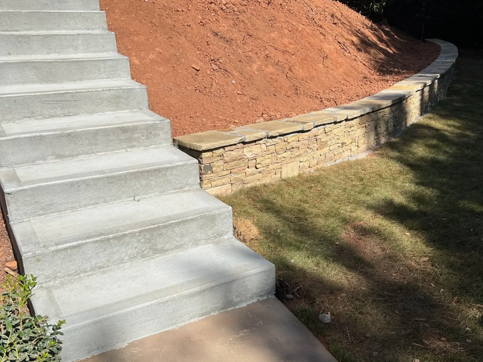 Concrete steps leading to a landscaped hill with stone retaining wall and manicured lawn, showcasing outdoor design.