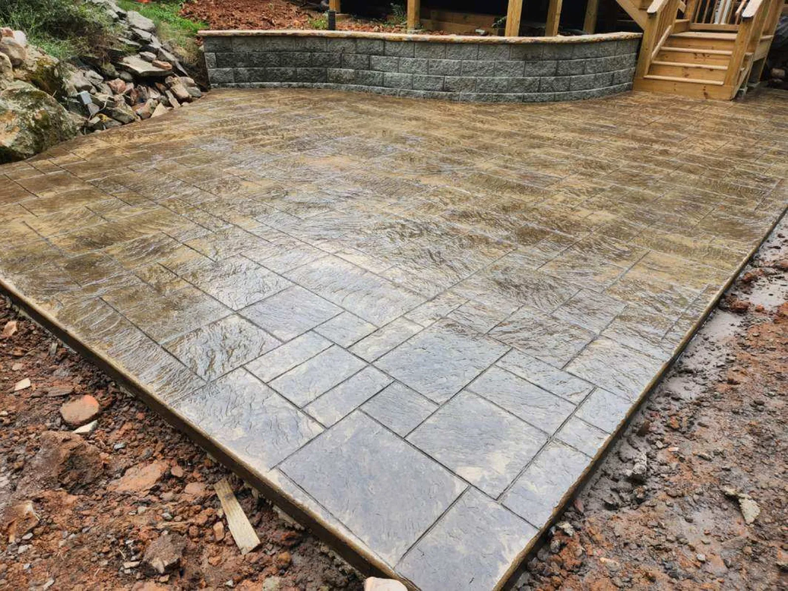 Newly installed stamped concrete patio with textured finish and curved edge, surrounded by natural stone.