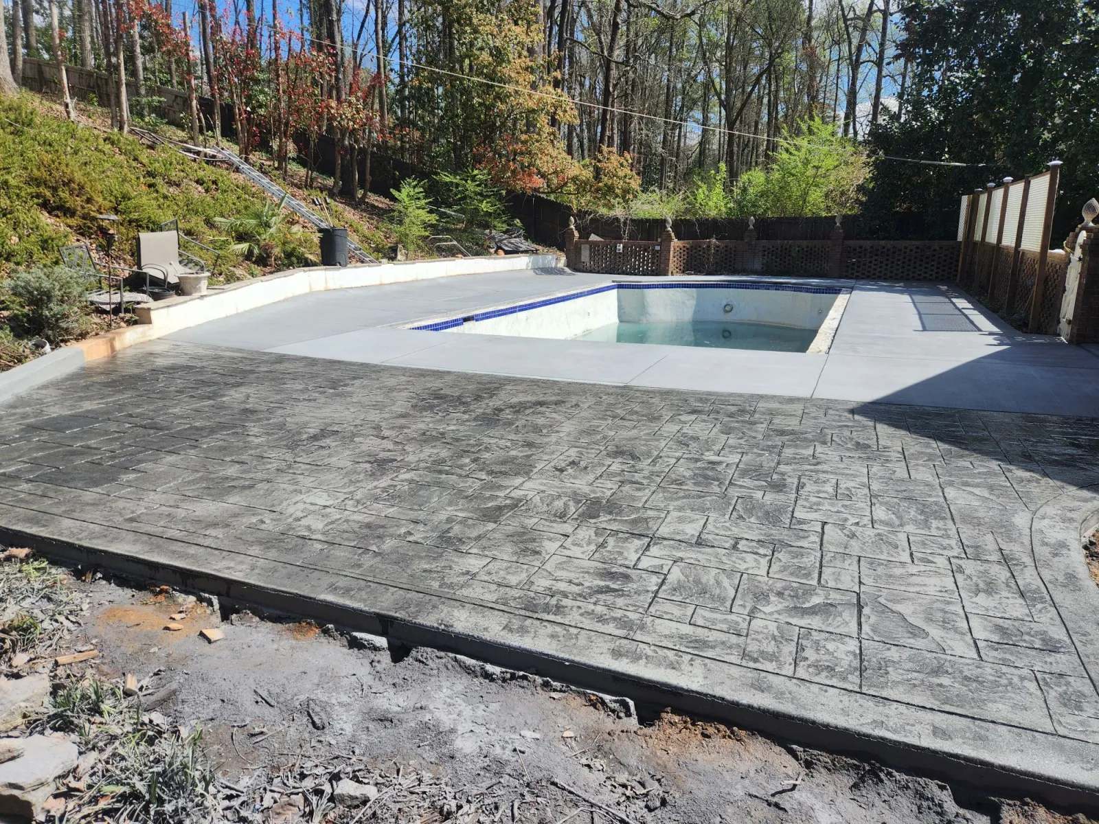 Stylish backyard pool with stamped concrete patio and lush greenery in a serene setting.