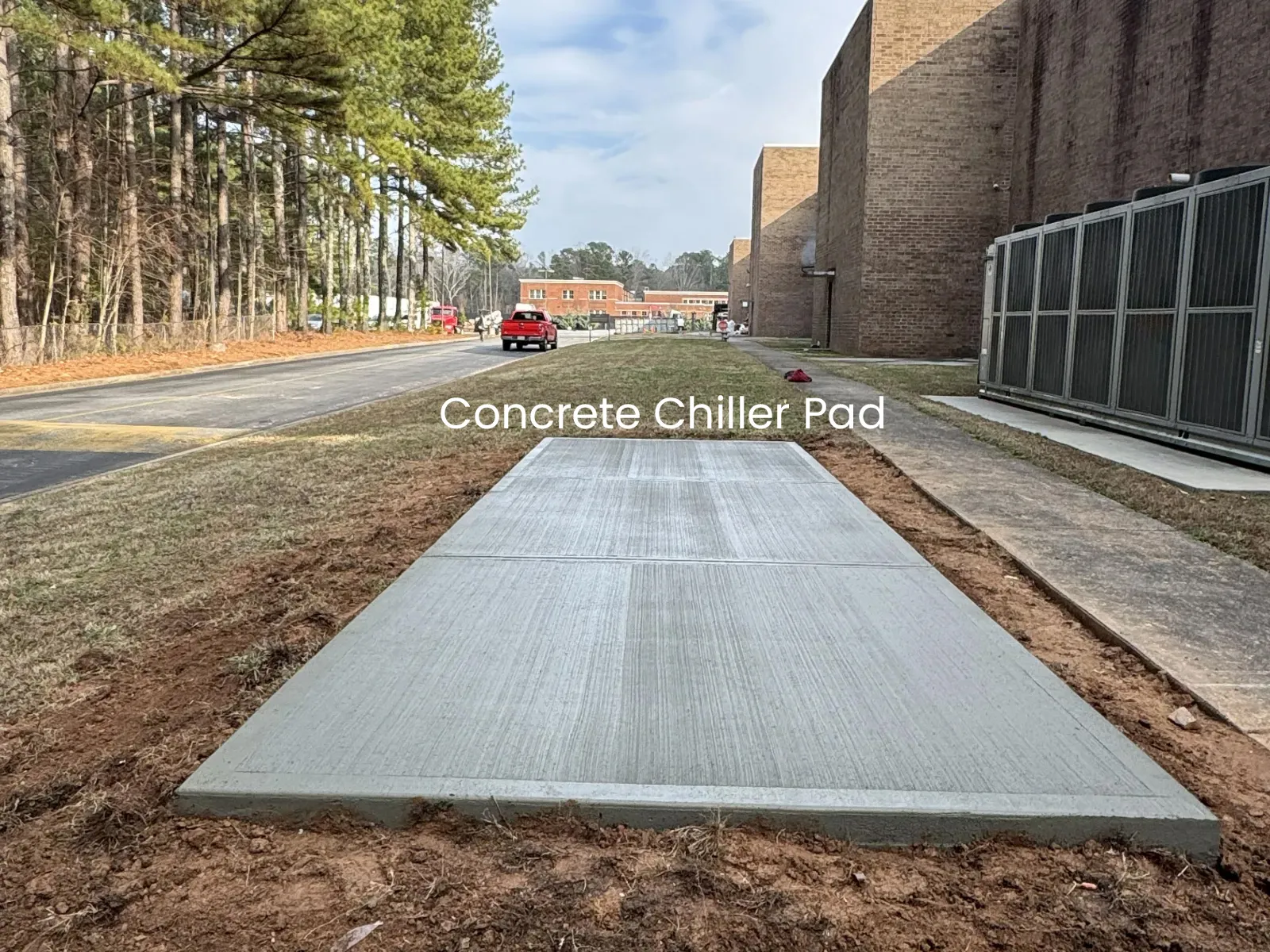 Newly poured concrete chiller pad installed outdoors near industrial building and road with trees