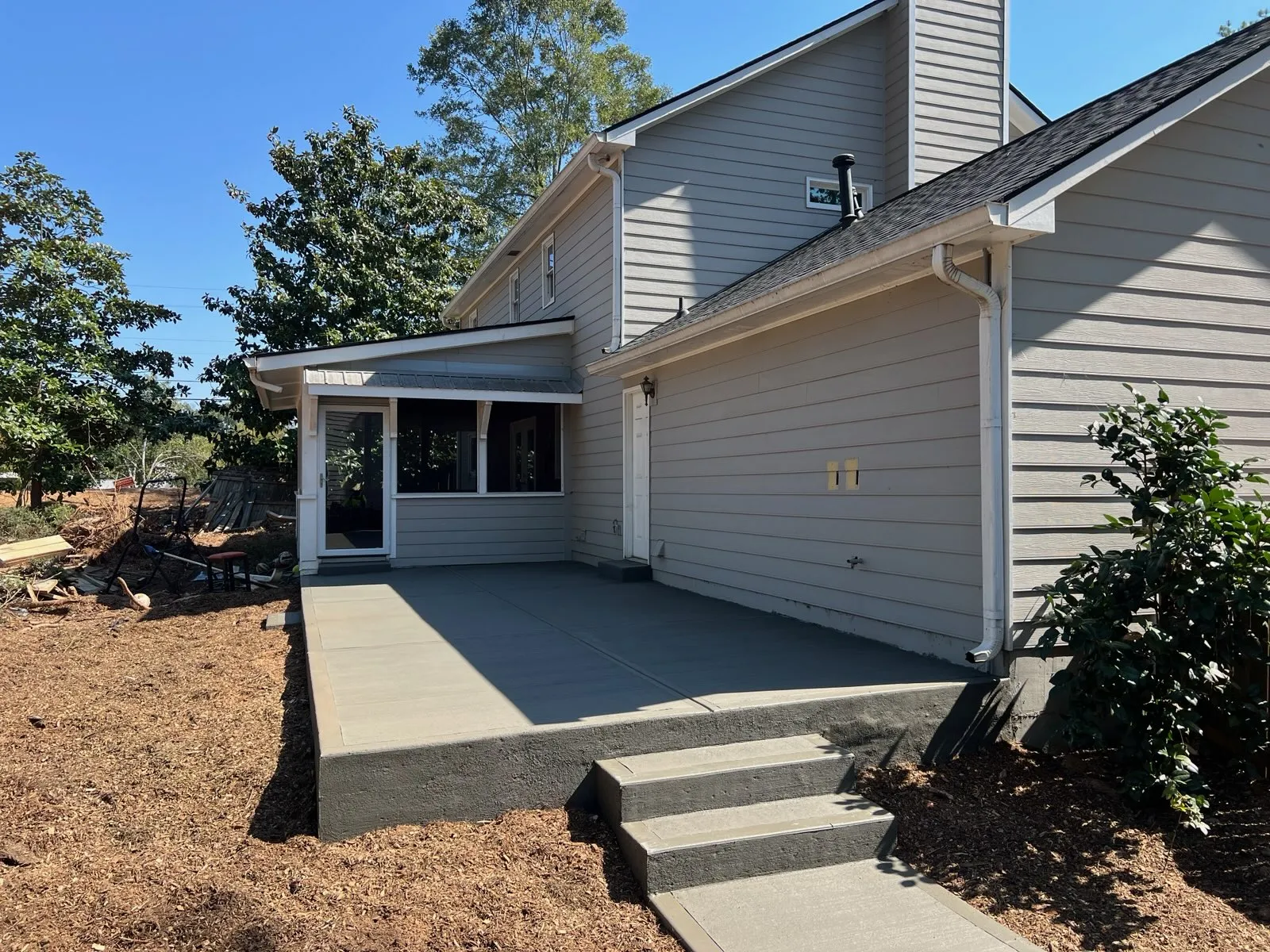 Modern home exterior with a spacious patio and clear blue sky, surrounded by trees and landscaping.