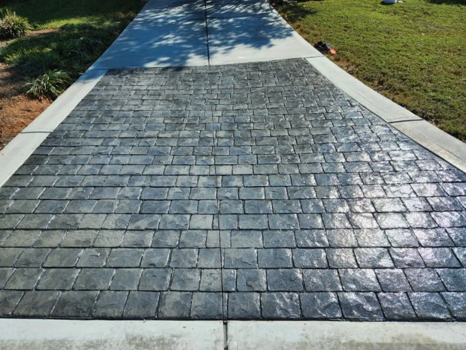 Stamped concrete driveway with a textured stone pattern and smooth concrete border under sunlight.