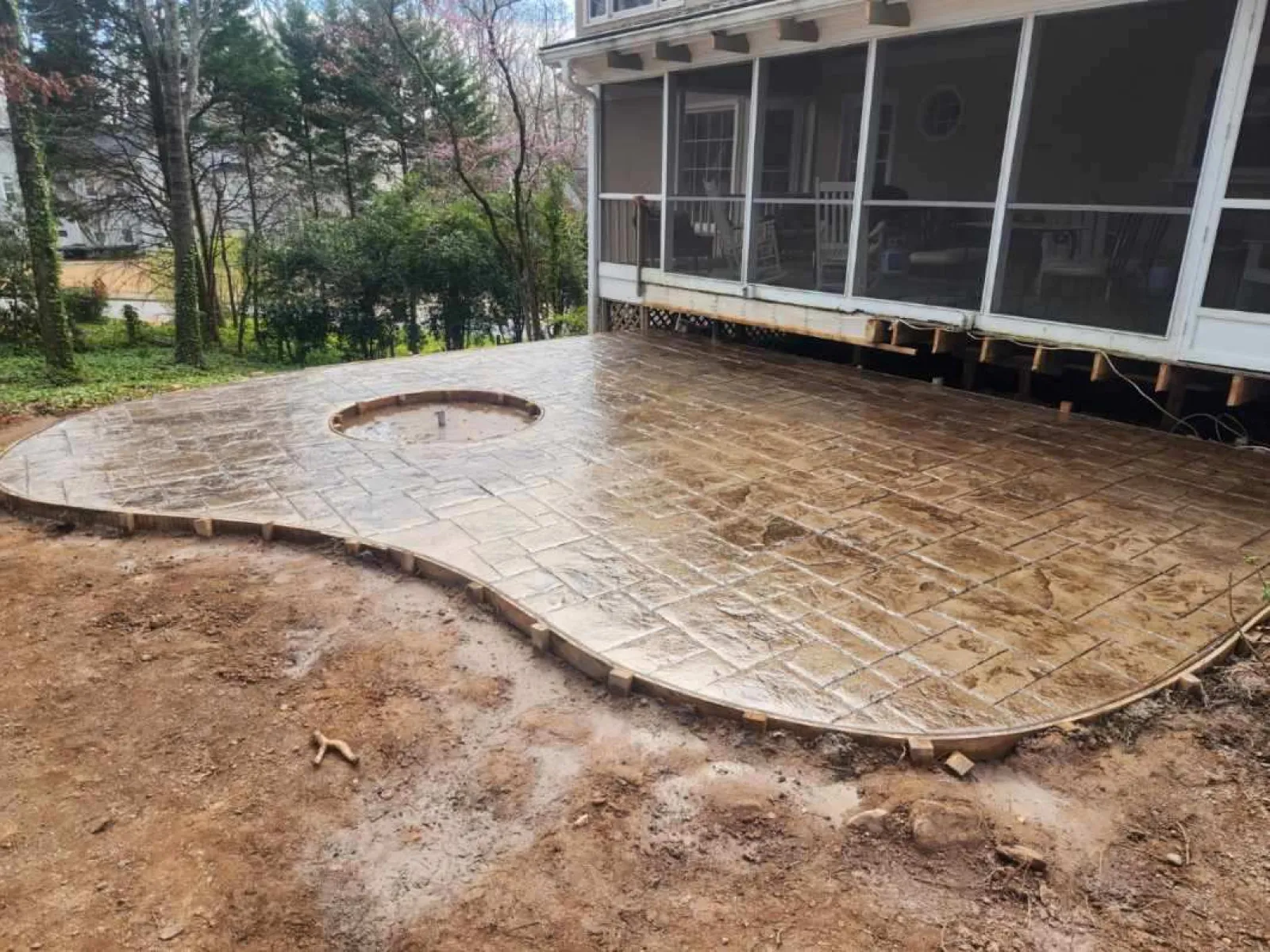 Freshly poured stamped concrete patio with circular design, surrounded by greenery and a covered porch area.