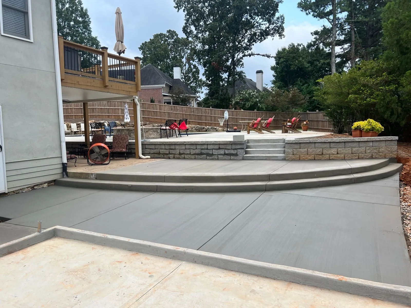 A modern outdoor space featuring a newly poured concrete patio, steps, and lounge chairs under a cloudy sky.