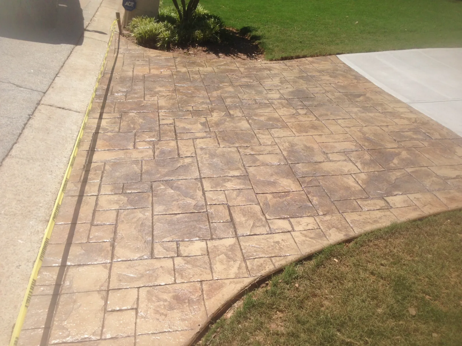 Decorative stamped concrete driveway with patterned design surrounded by grass and garden bed.