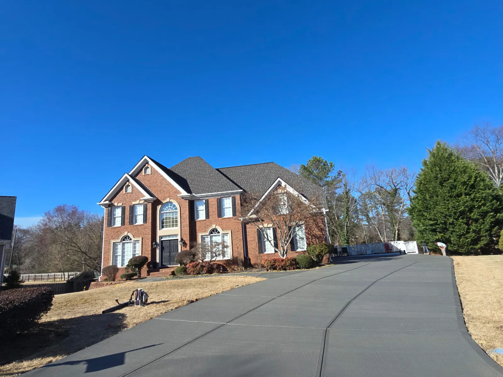 Spacious brick two-story house with a large clean concrete driveway under a clear blue sky.